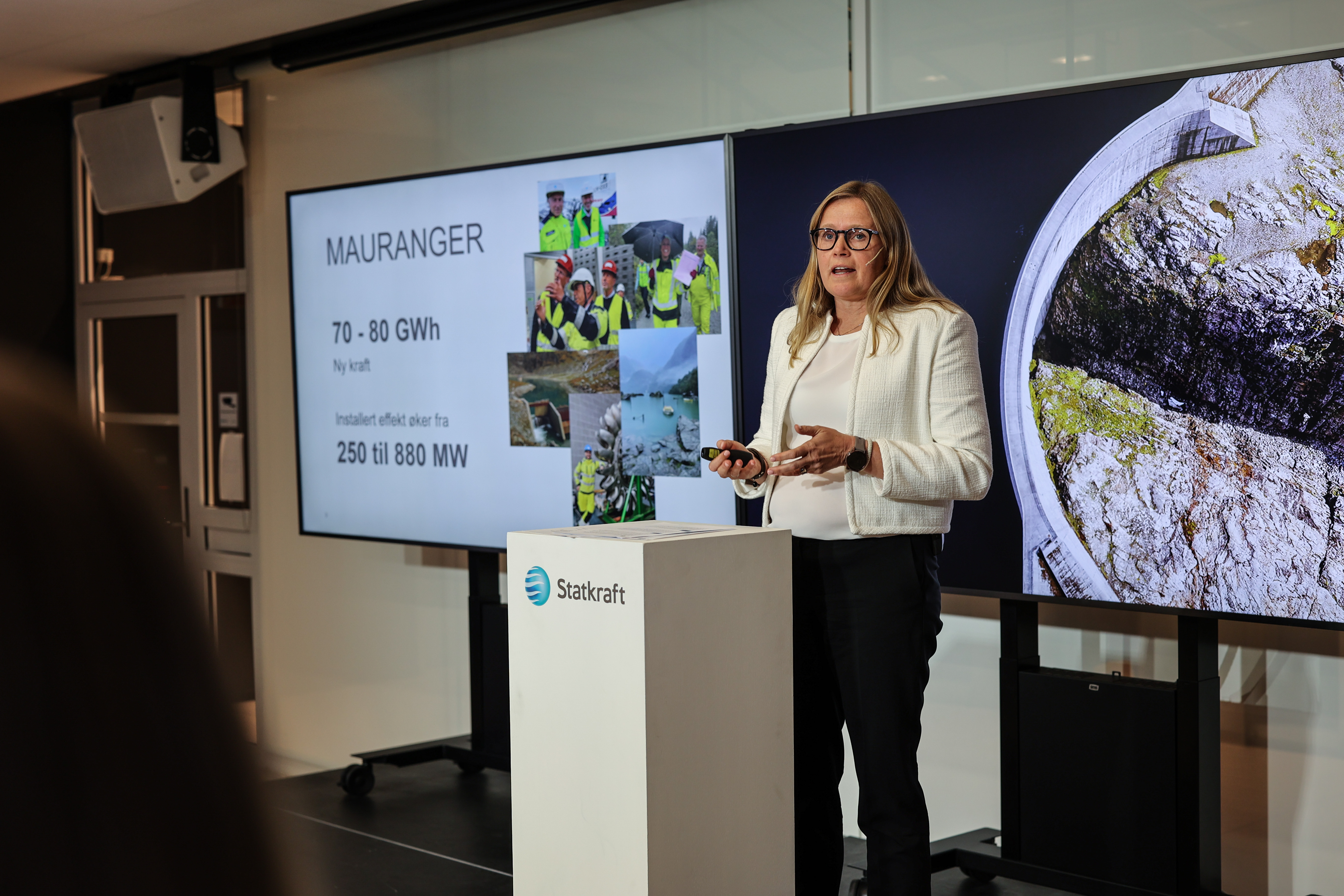 Woman presenting on a podium in front of two tv screens